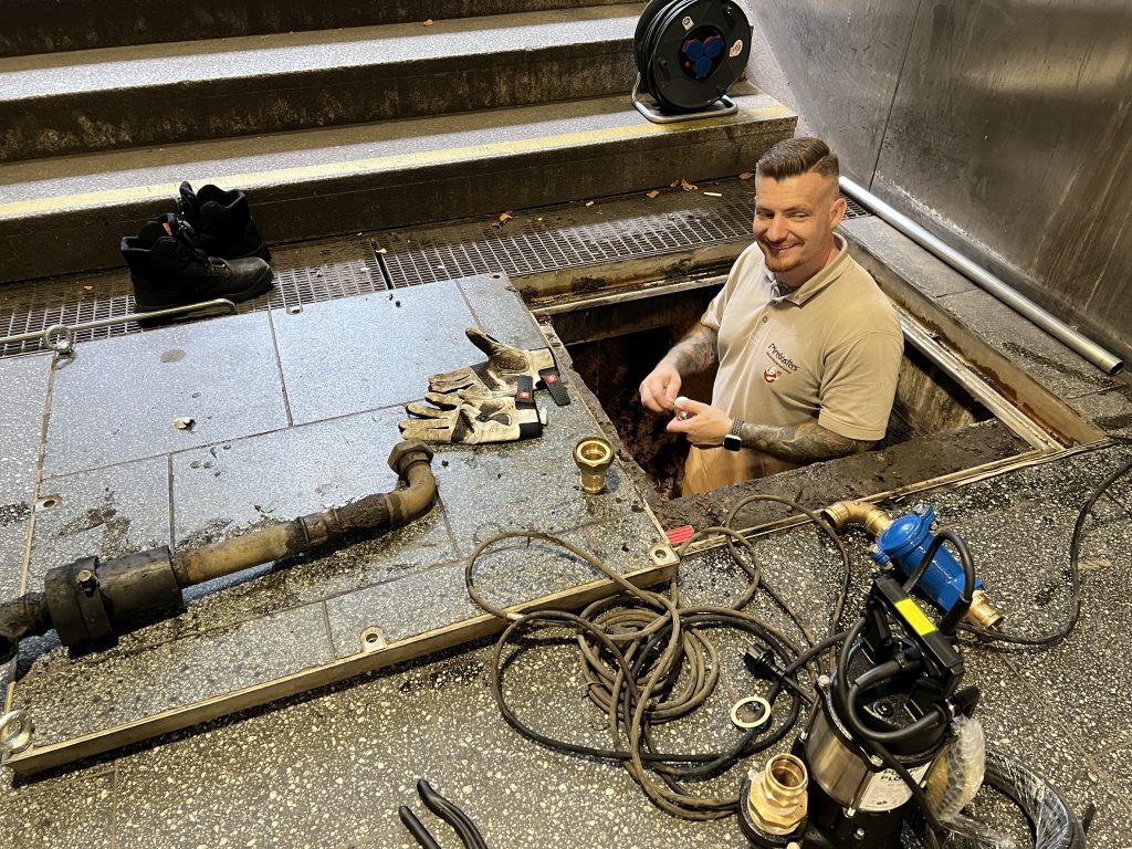 Ein Pipebusters-Techniker arbeitet in einer geöffneten Abwassergrube und führt Wartungsarbeiten durch.