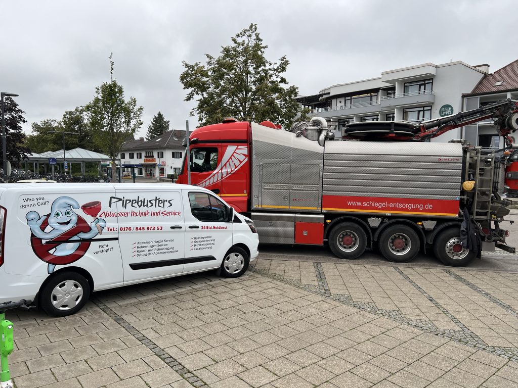 Ein Pipebusters Servicefahrzeug steht neben einem großen Entsorgungs-Lkw auf einem öffentlichen Platz in München.