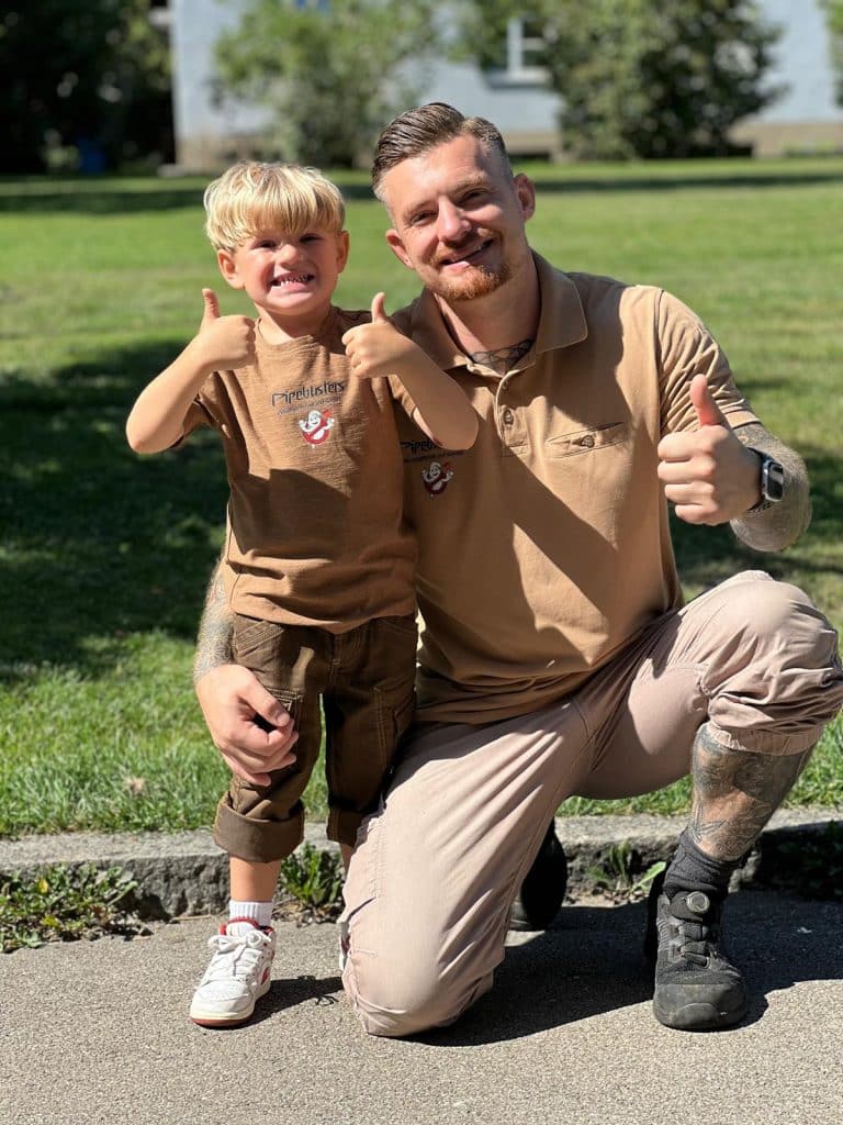 Ein Pipebusters-Mitarbeiter in Arbeitskleidung posiert lächelnd mit einem Kind im Freien.